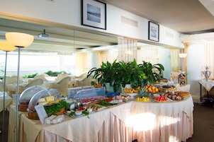 Mesa de buffet com diversos alimentos e uma grande planta em vaso.