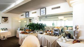 A dining area with multiple tables set for breakfast, featuring a variety of food items and a coffee station.
