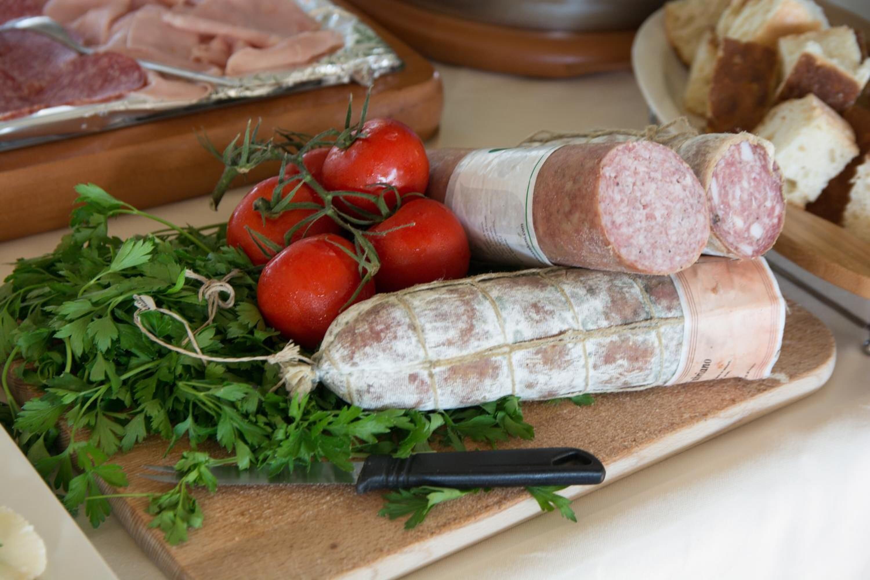 Ein Holzschnittbrett mit geschnittenen Wurstscheiben, frischen Tomaten und Petersilie.