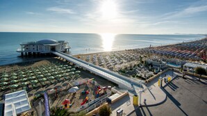 Un resort frente a la playa con una piscina grande, sombrillas y un puente que da acceso a la playa.