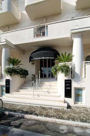 A hotel entrance with a grand staircase, a black awning, and potted plants.