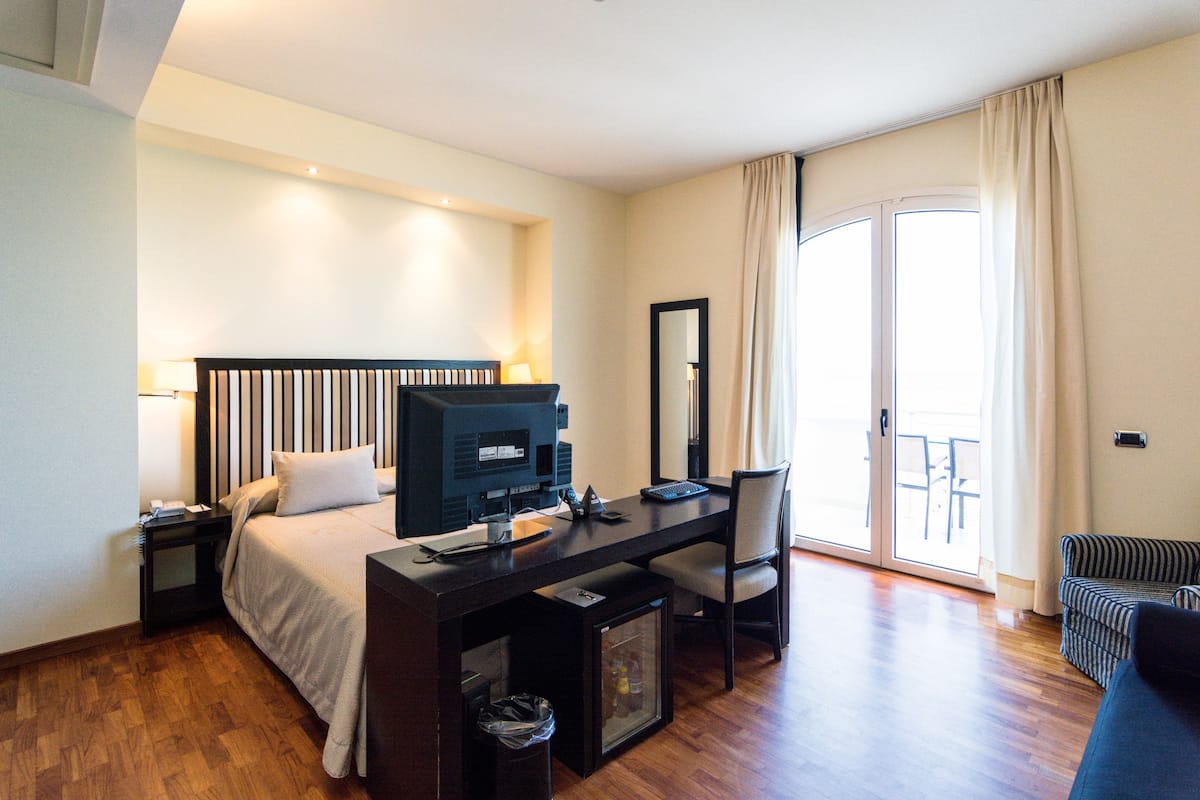 Habitación de hotel con cama, escritorio, silla y vista al exterior a través de una puerta corredera.