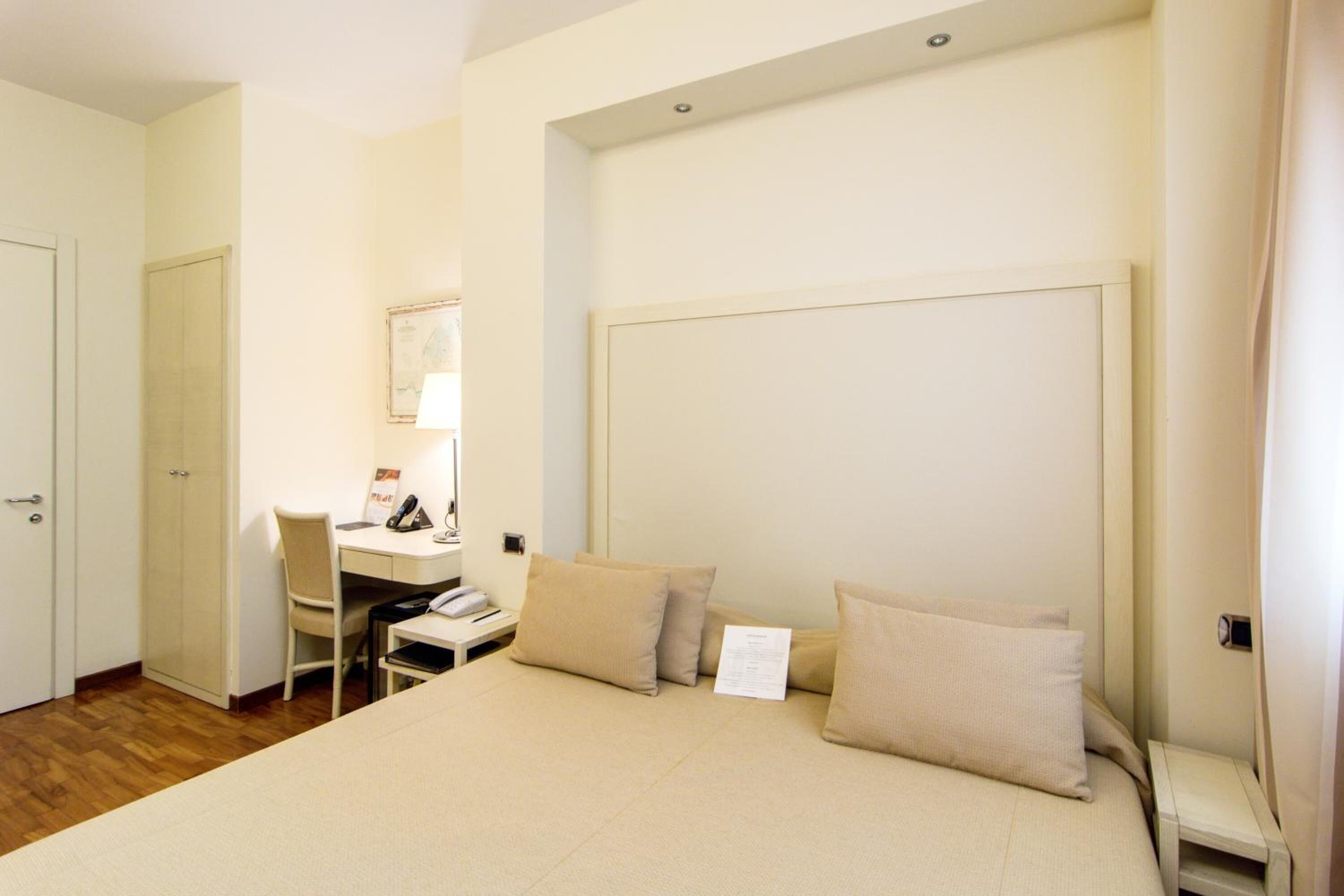A hotel room with a bed, a desk, a chair, and a wardrobe.