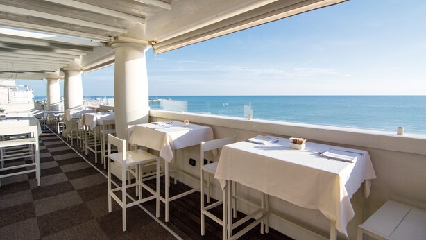 Un restaurante con mesas y sillas blancas, piso a cuadros y vista al mar.
