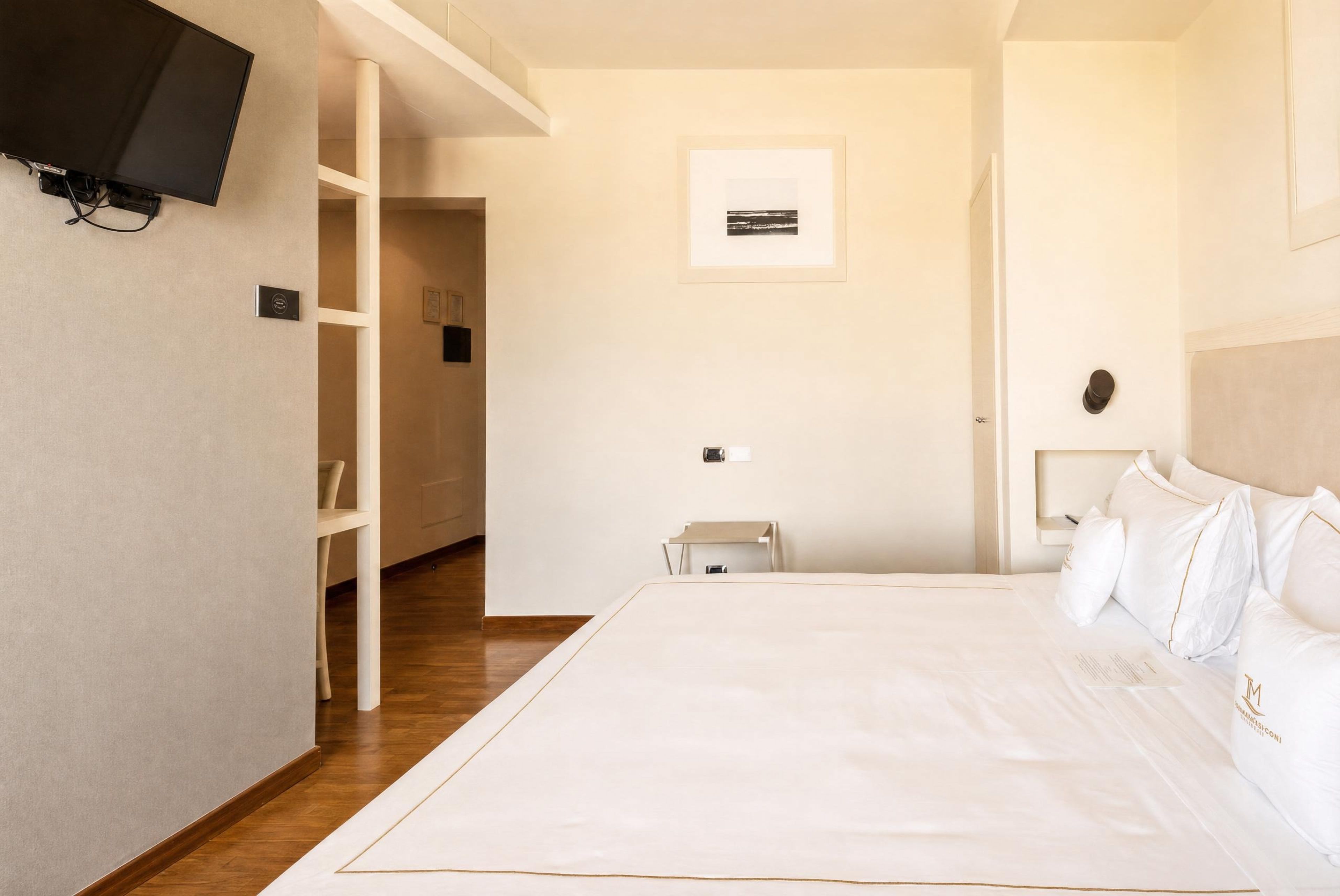 Habitación de hotel con una cama grande, un televisor de pantalla plana montado en la pared, piso de madera e imagen enmarcada en la pared.