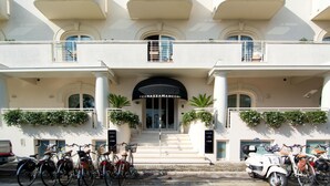 Un hotel de varios pisos con una entrada destacada, asientos al aire libre y una variedad de bicicletas estacionadas adelante.