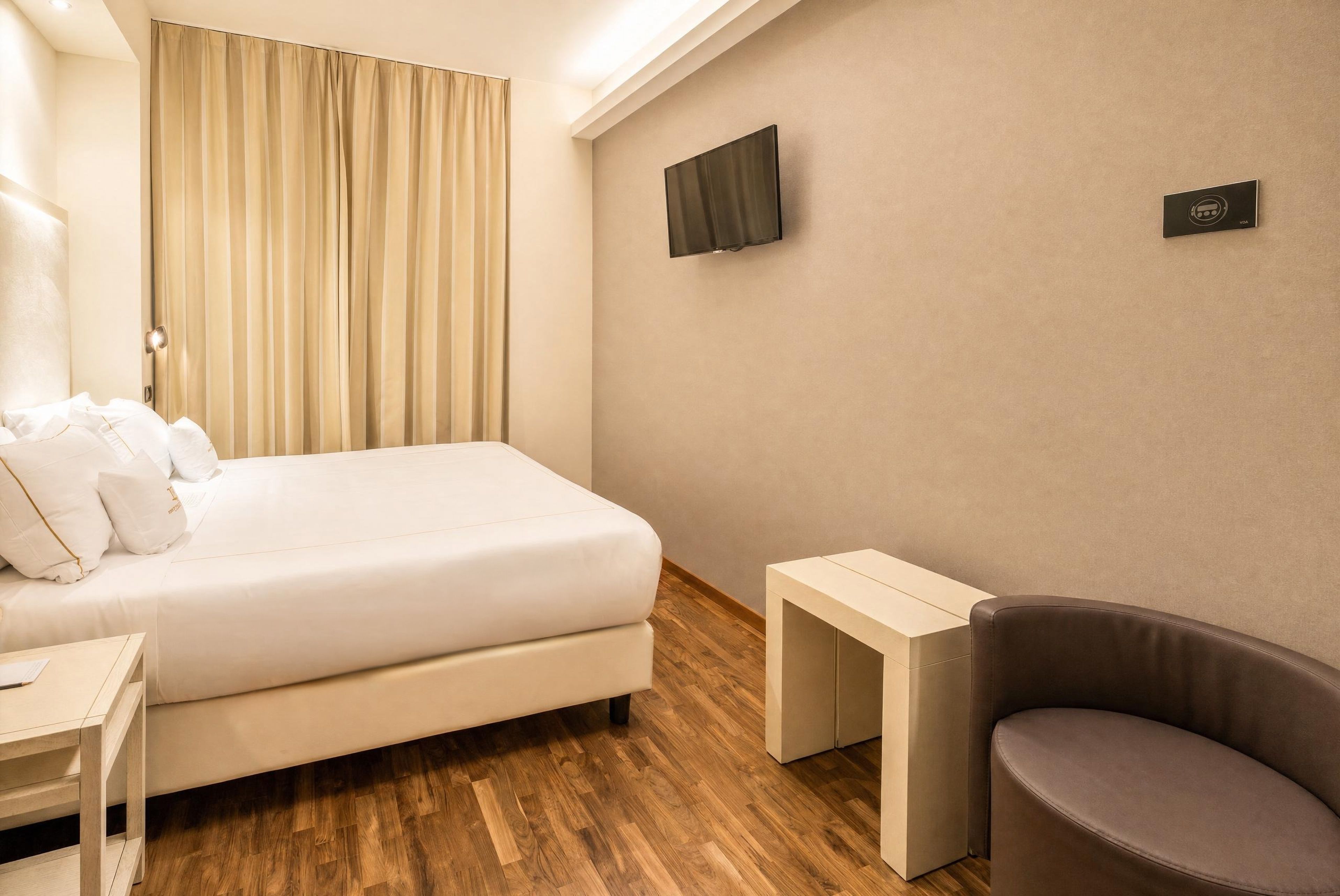 A hotel room with a bed, a small table, a chair, a TV, and a sign on the wall.