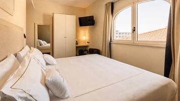 A hotel room with a large bed, a wardrobe, a TV mounted on the wall, and a window with curtains.