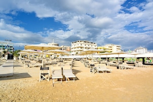 Un hotel frente a la playa con varios niveles, zonas de estar al aire libre y sombrillas.