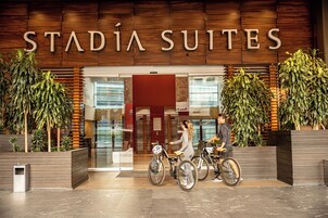 La entrada de Stadia Suites, con un diseño moderno, presenta un revestimiento de madera y grandes macetas con plantas.