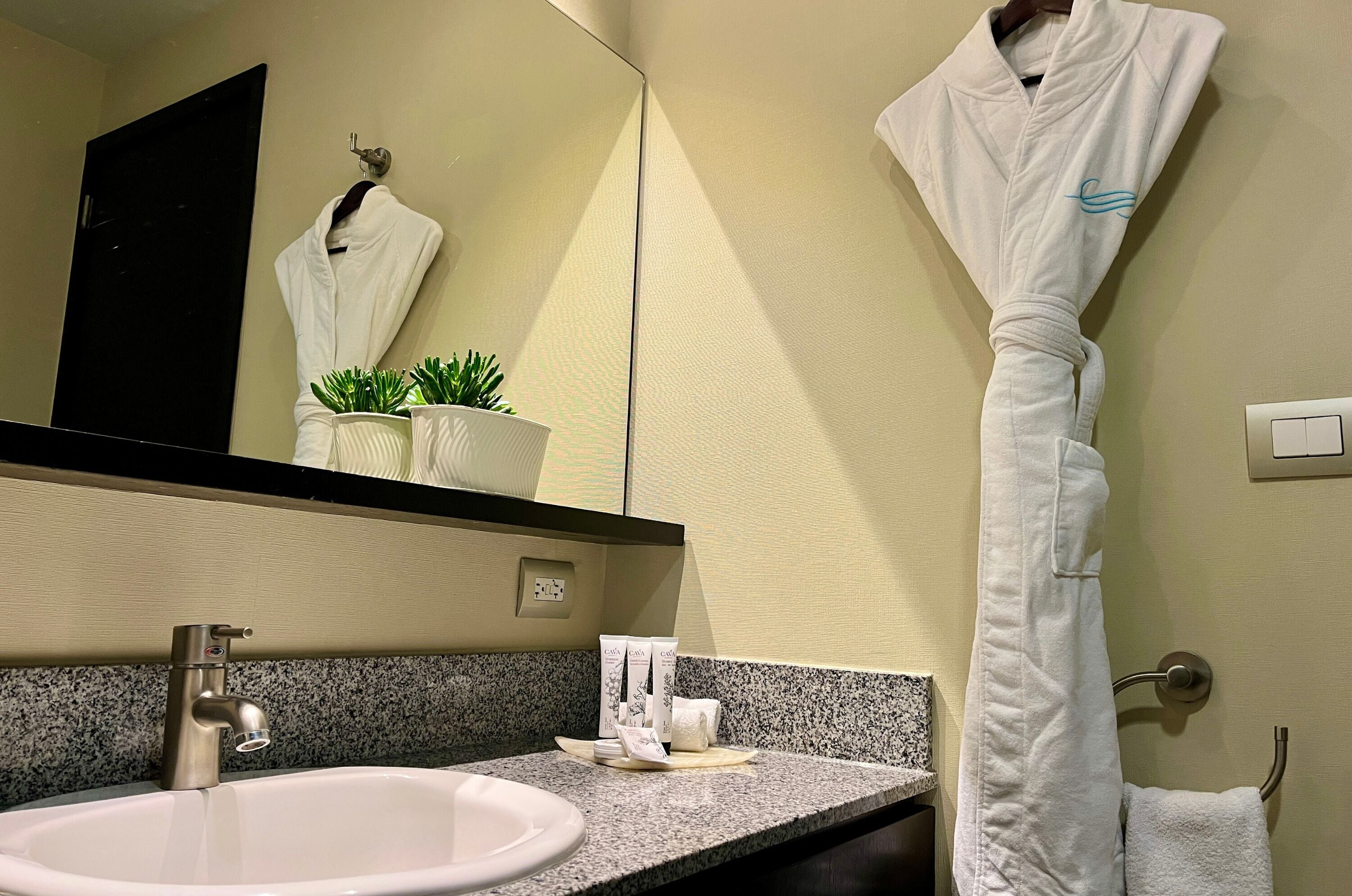 A bathroom with a sink, mirror, towel rack, and a robe hanging on the wall.