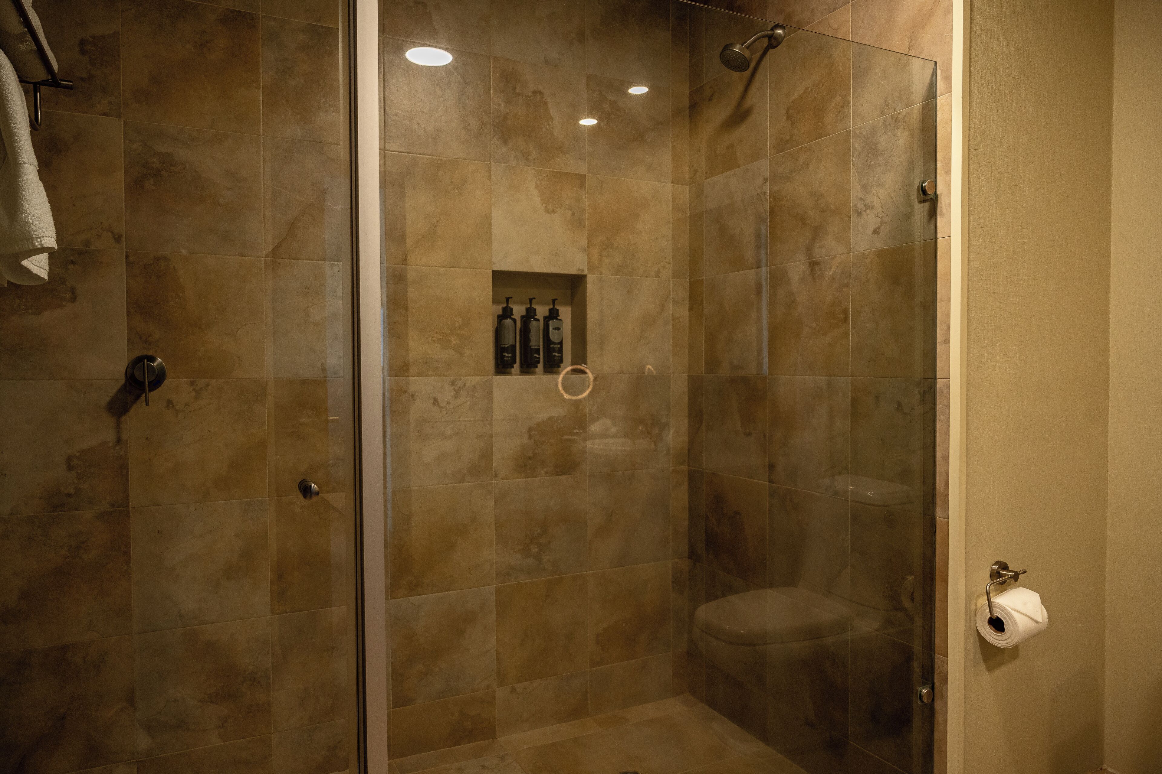 A glass-enclosed shower with beige tiles, a toilet, and a towel rack.