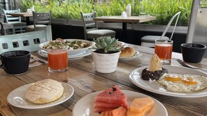 A breakfast table with plates of food, drinks, and a view of greenery outside. - Stadía Suites Mexico City Santa Fe (Mexico City)