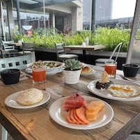 Una mesa de desayuno con platos de comida, bebidas y vistas al verdor exterior.