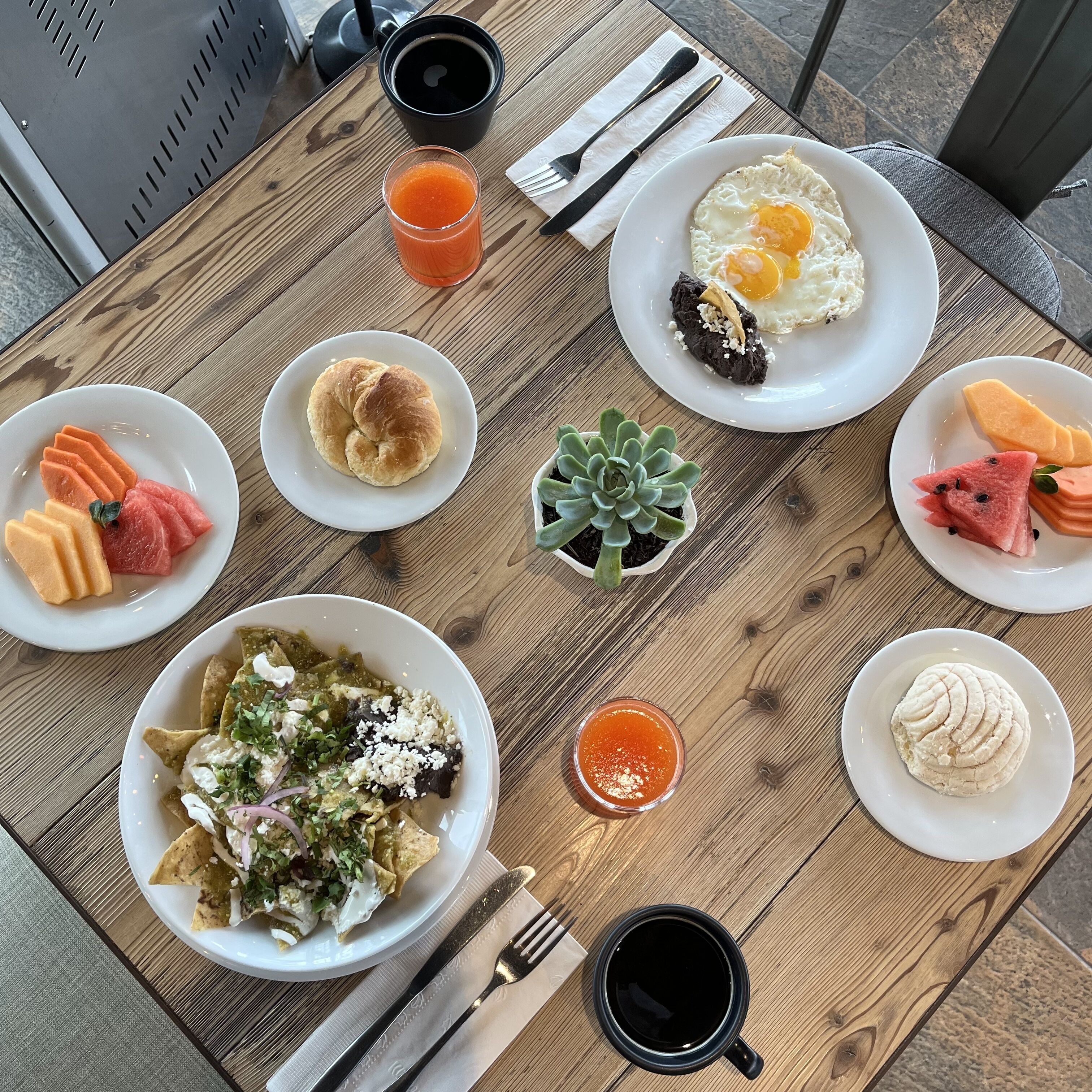 A wooden table with various breakfast items including eggs, pancakes, and fresh fruit.