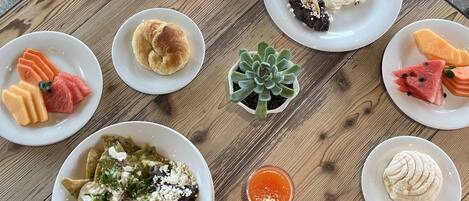 A wooden table with various breakfast items including eggs, pancakes, and fresh fruit.