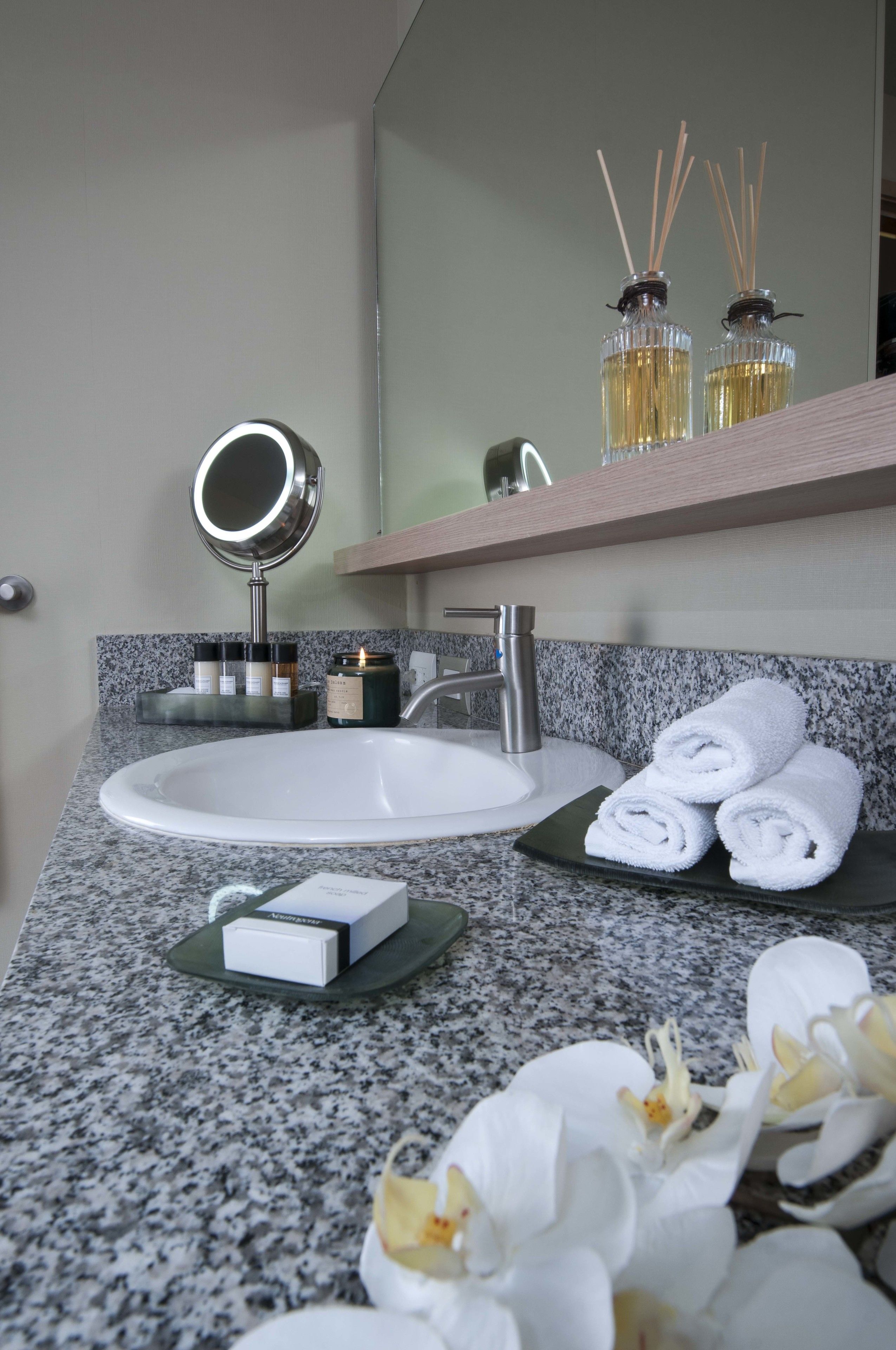A bathroom with a granite countertop, a white sink, a mirror, and a towel rack with folded towels.