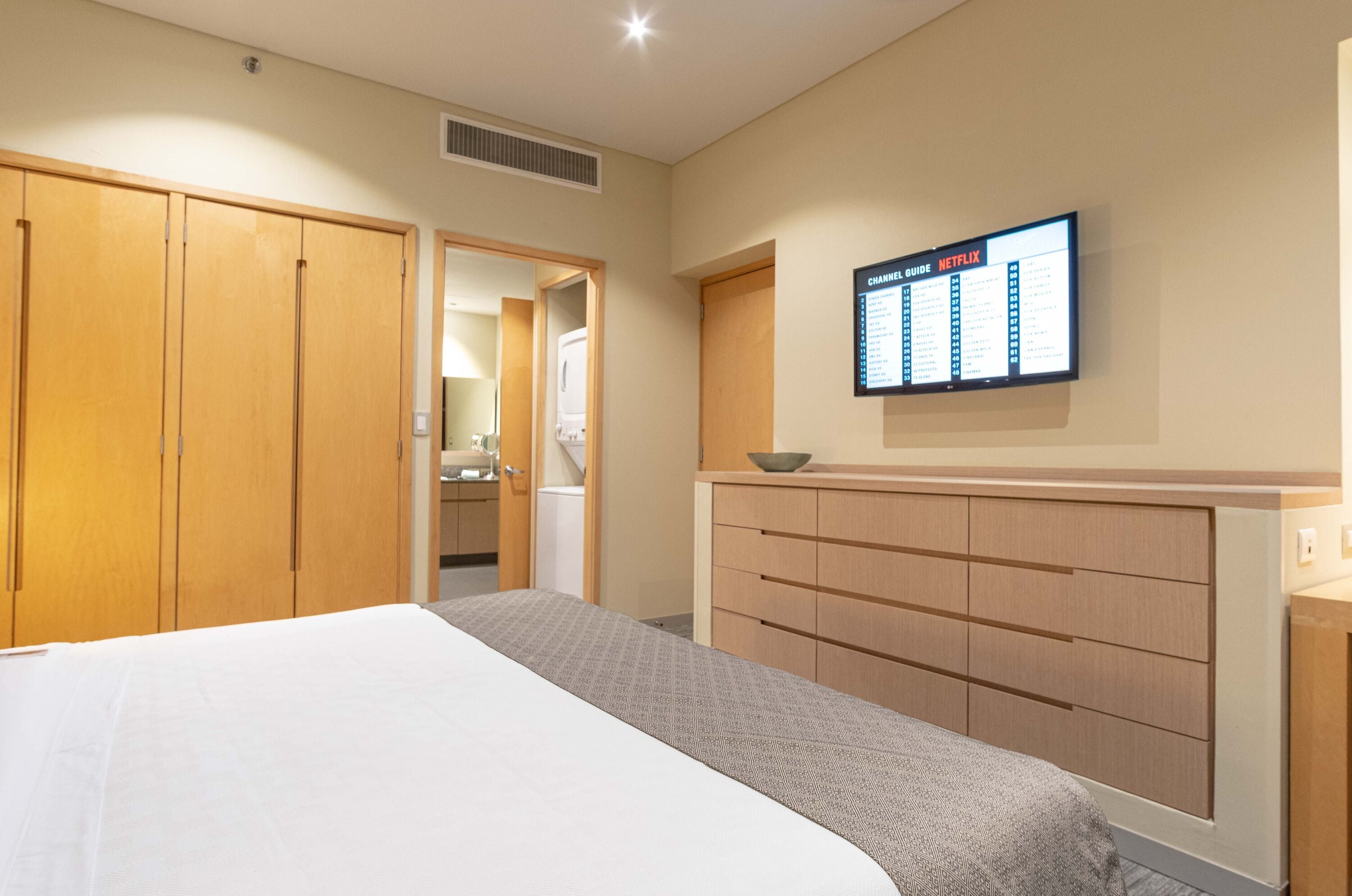A hotel room with a bed, wooden wardrobe, a TV mounted on the wall displaying a Netflix guide, and a small bedside table.