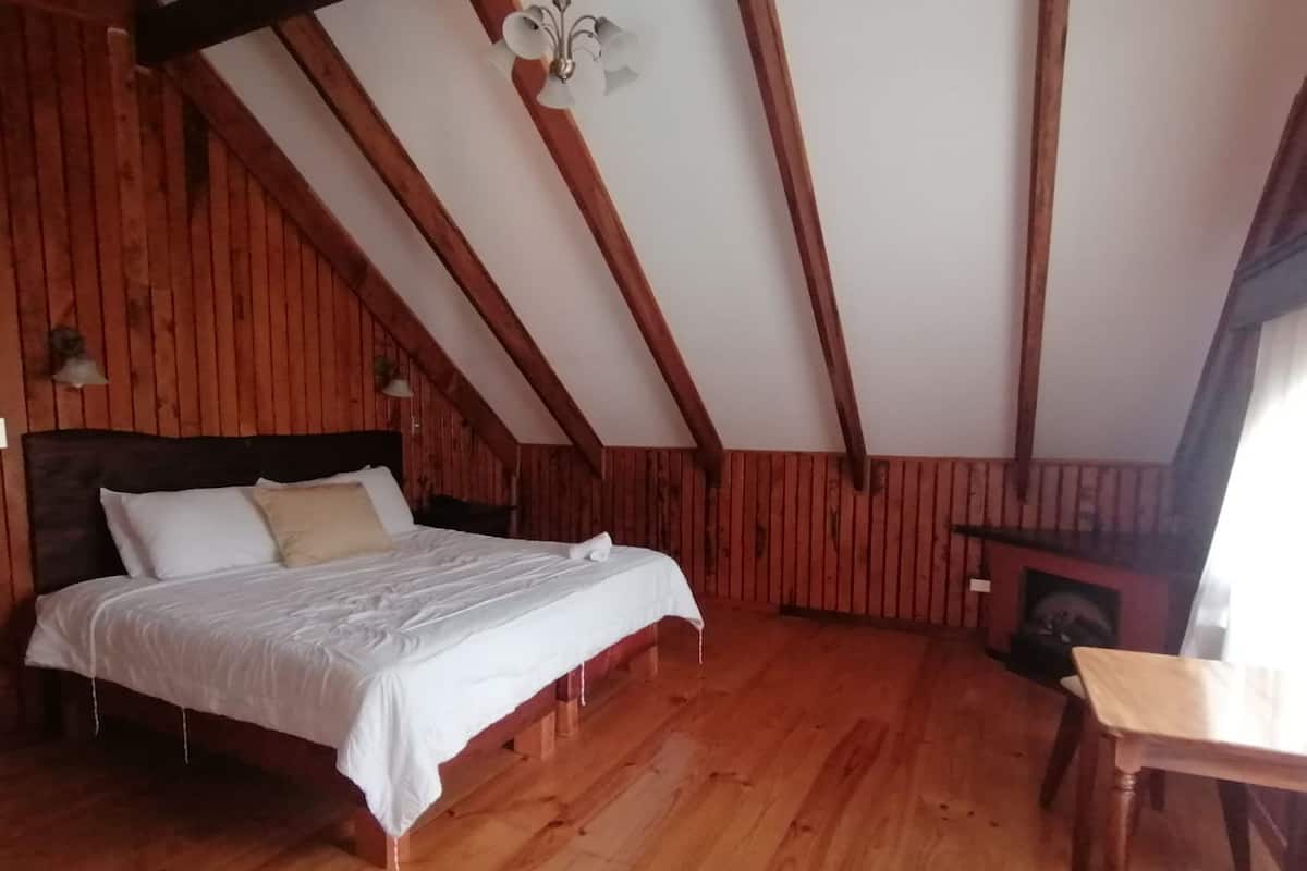 A wooden-paneled room with a bed, a table, and a fireplace.