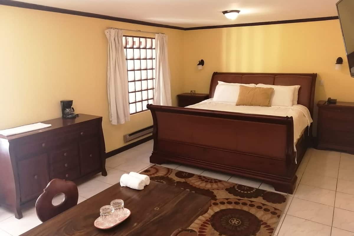 A hotel room with a wooden bed, a desk with a chair, a small table with a tray, and a window with curtains.