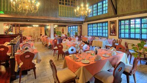A spacious dining area with multiple tables set for guests, large windows allowing natural light, and a chandelier hanging from the ceiling. - Hotel El Tirol (Ángeles)