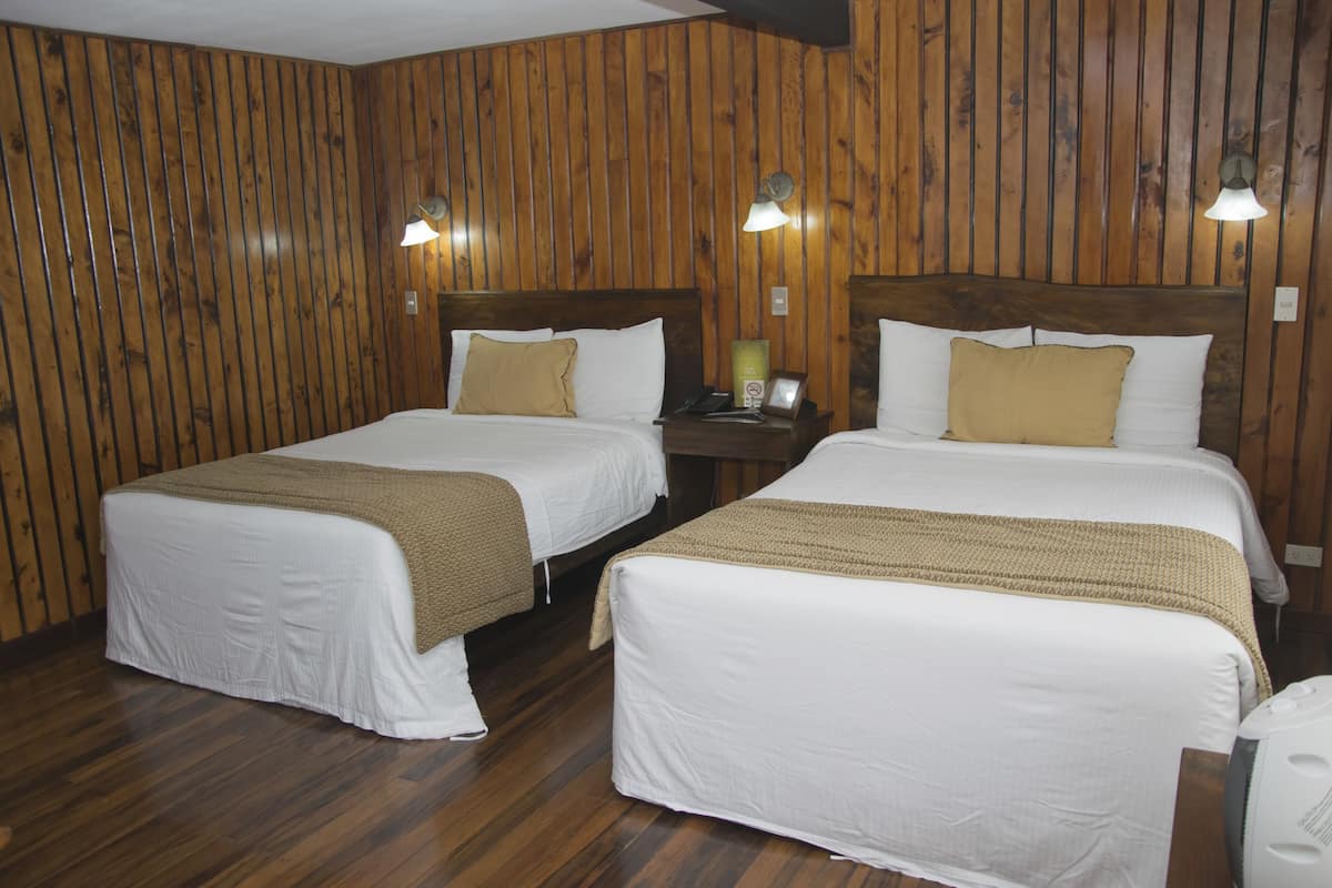 A hotel room with two beds, wooden panel walls, and bedside lamps.