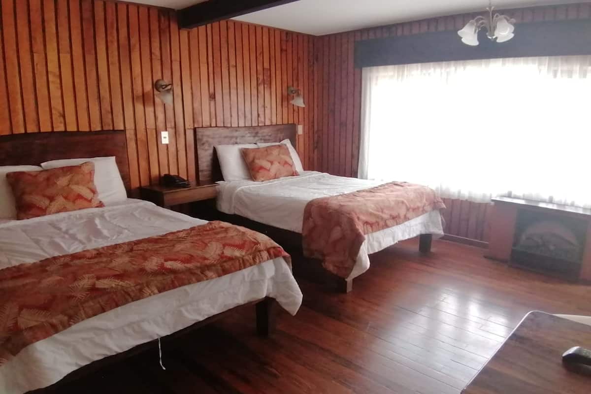 A room with two beds, wooden walls, a chandelier, and a fireplace.