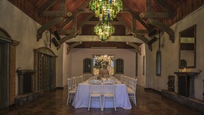A large dining hall with a long table set for a banquet, wooden beams on the ceiling, and a fireplace on the right. - Hotel El Tirol (Ángeles)