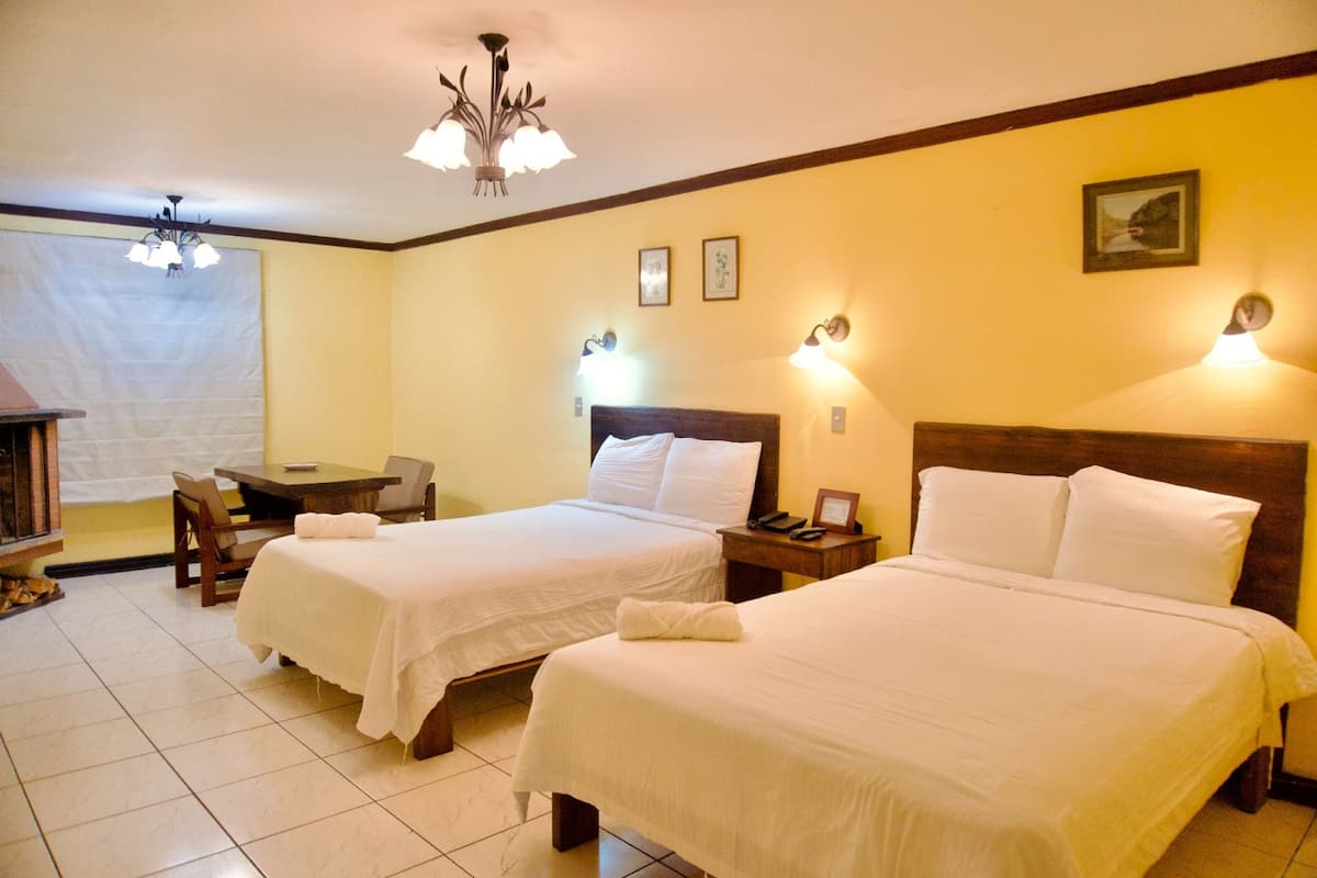 A hotel room with two beds, a small table, and a chair.