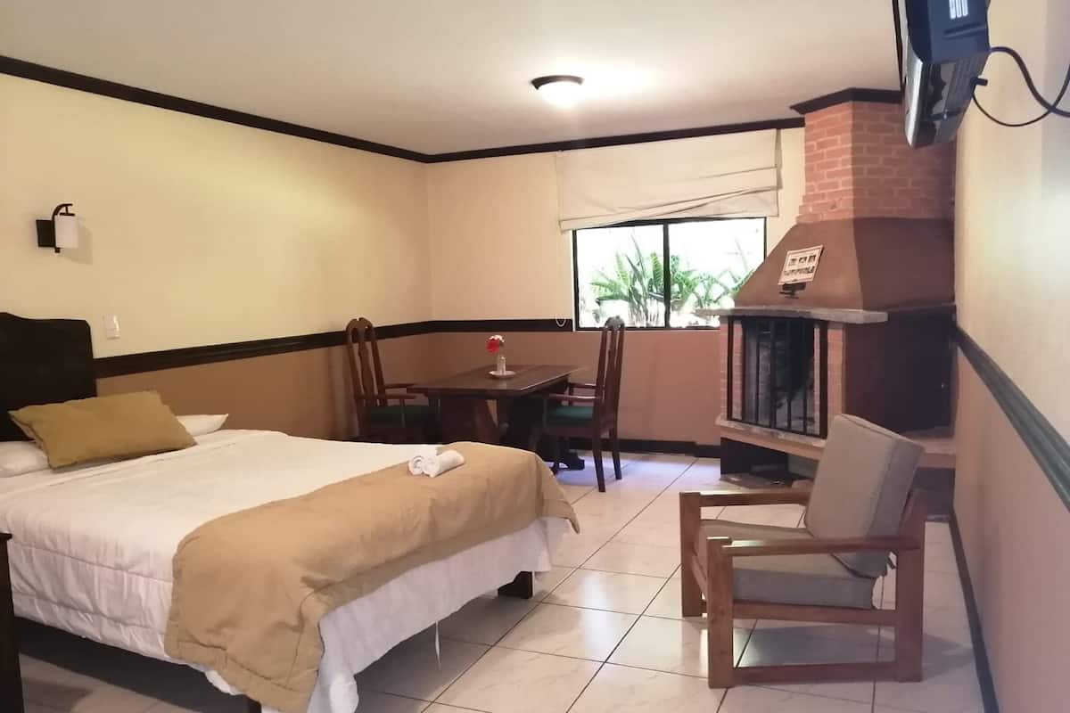 A hotel room with a bed, a small dining table, a chair, and a fireplace.