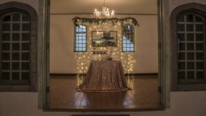 A room with a chandelier, a table covered with a golden cloth, and two windows with curtains. - Hotel El Tirol (Ángeles)