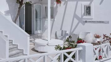 Um edifício branco com área de estar coberta ao ar livre, uma escadaria e uma pequena janela com grade metálica decorativa.