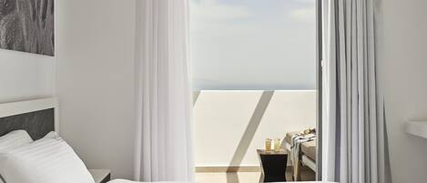 A hotel room with a bed, a nightstand, a small table with drinks, and a view of the sky through sheer curtains.