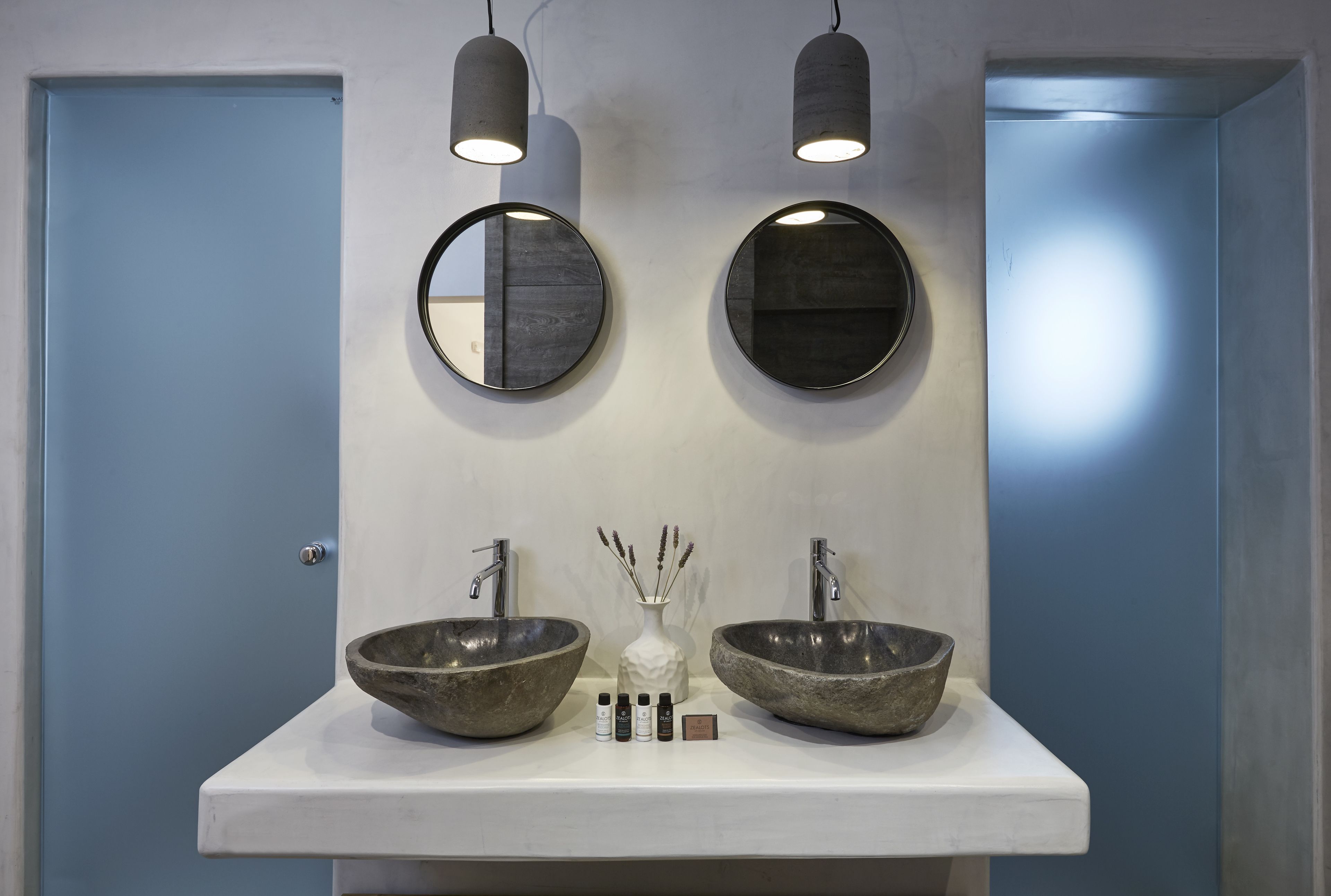 A bathroom with two large stone sinks, a white countertop, and two round mirrors.