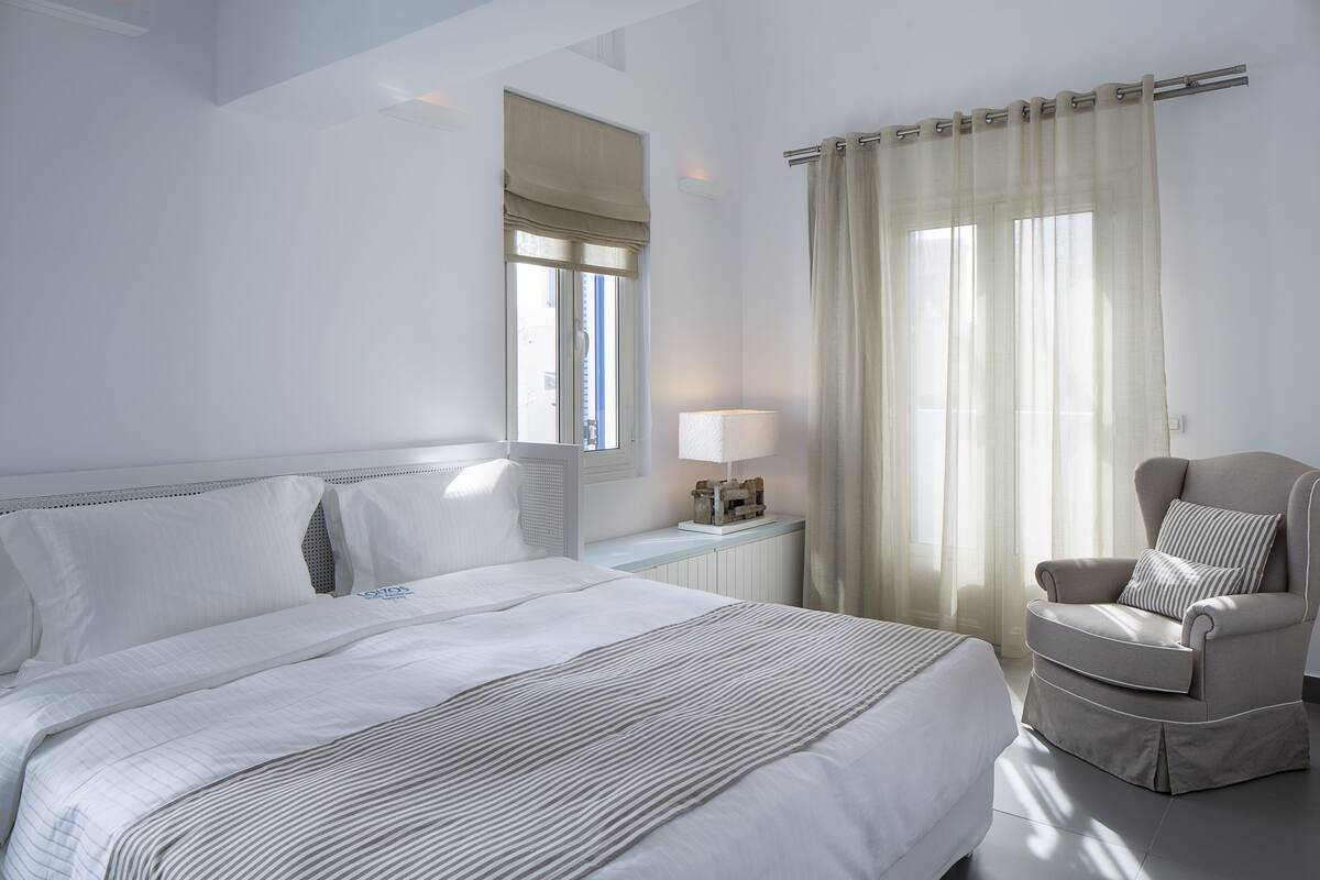 A hotel room with a large bed, a chair, a nightstand, and a window with curtains.