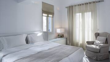 Una habitación de hotel con una cama grande, una silla, una mesita de noche y una ventana con cortinas.