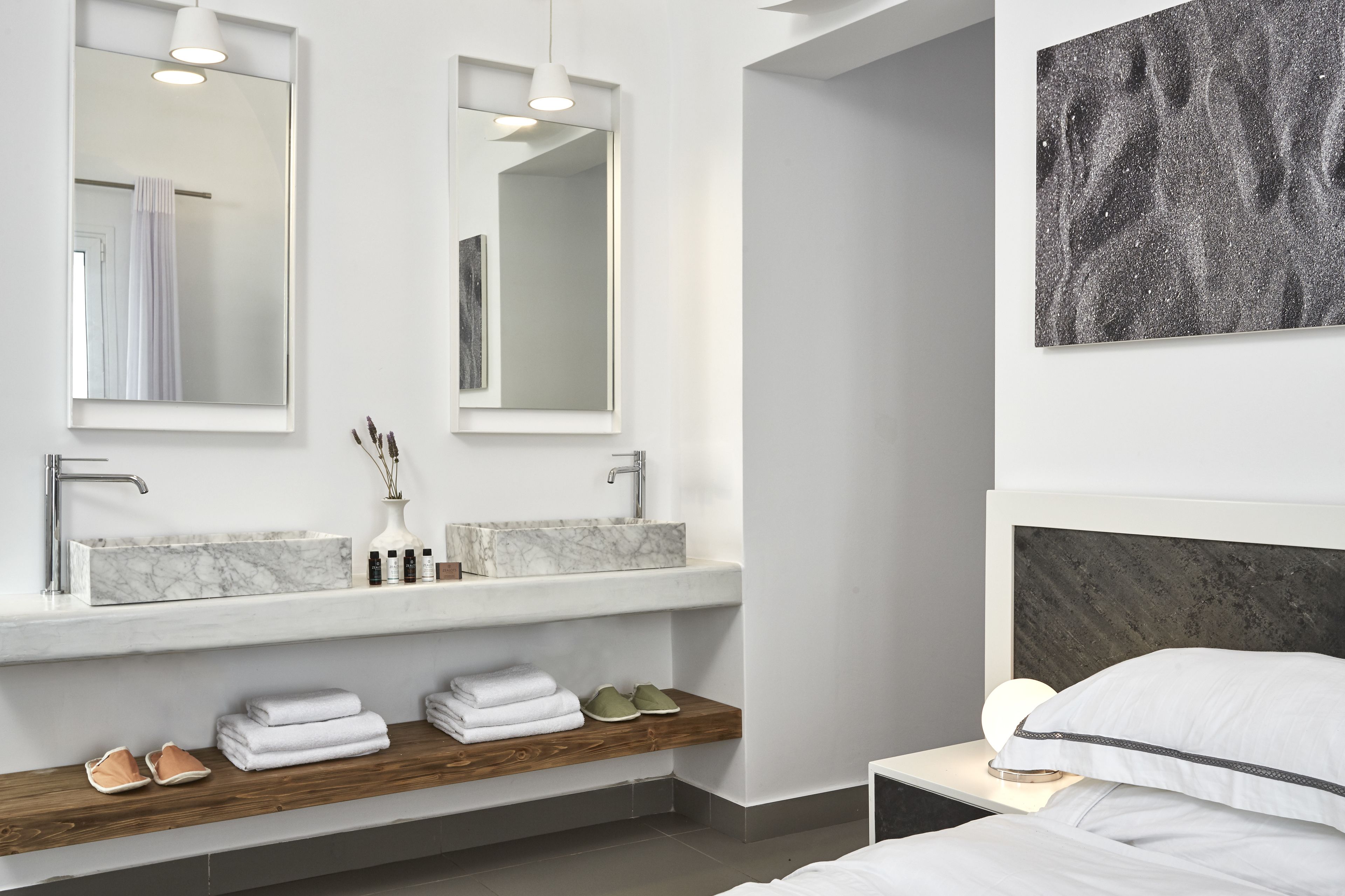 A modern bathroom with two marble sinks, a wooden shelf with towels and shoes, and a large mirror above the sink.