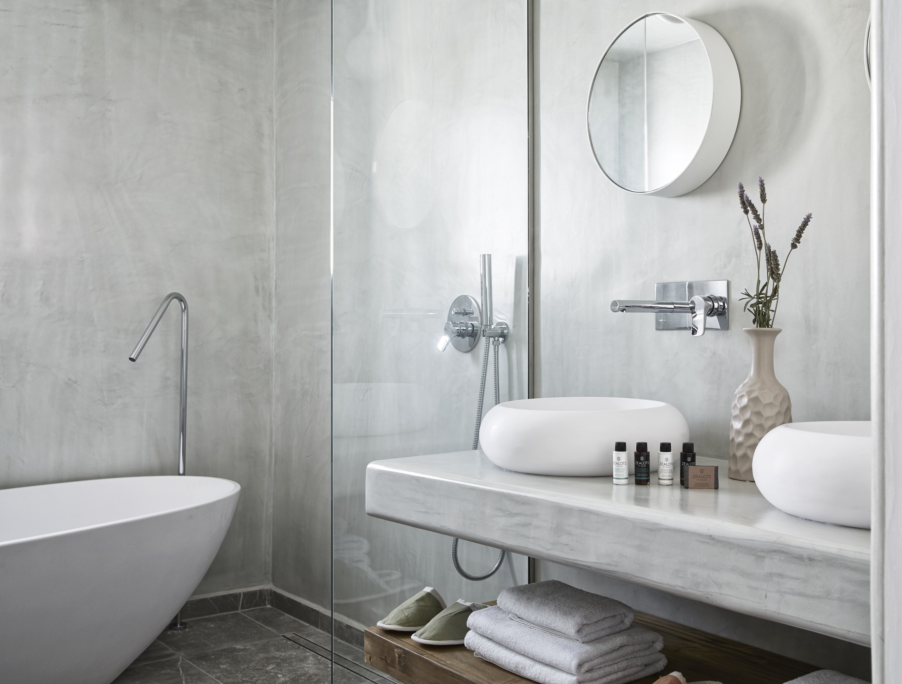 A modern bathroom with a freestanding bathtub, a glass-enclosed shower, and a marble vanity with a mirror and toiletries.