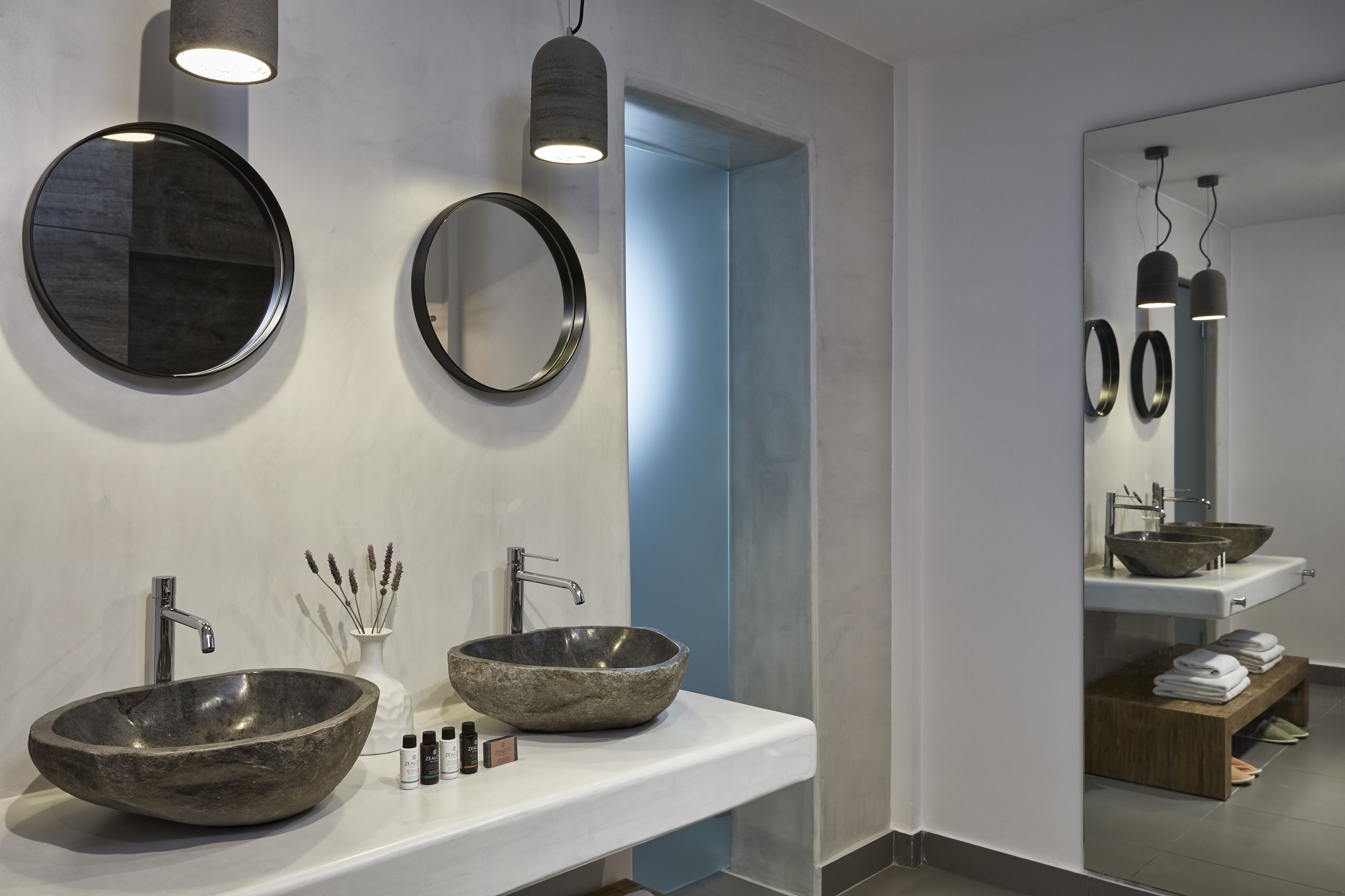 A modern bathroom with two large, round mirrors, a stone vessel sink, and a white countertop.