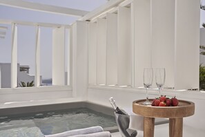 A modern indoor pool area with a wooden table holding a bottle of champagne and glasses, and a tray of strawberries. - Loizos Stylish Residences (Santorini)
