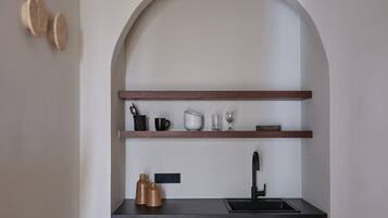 A kitchen with a black countertop, wooden cabinets, and a built-in sink. There are two shelves above the countertop holding various kitchen items.