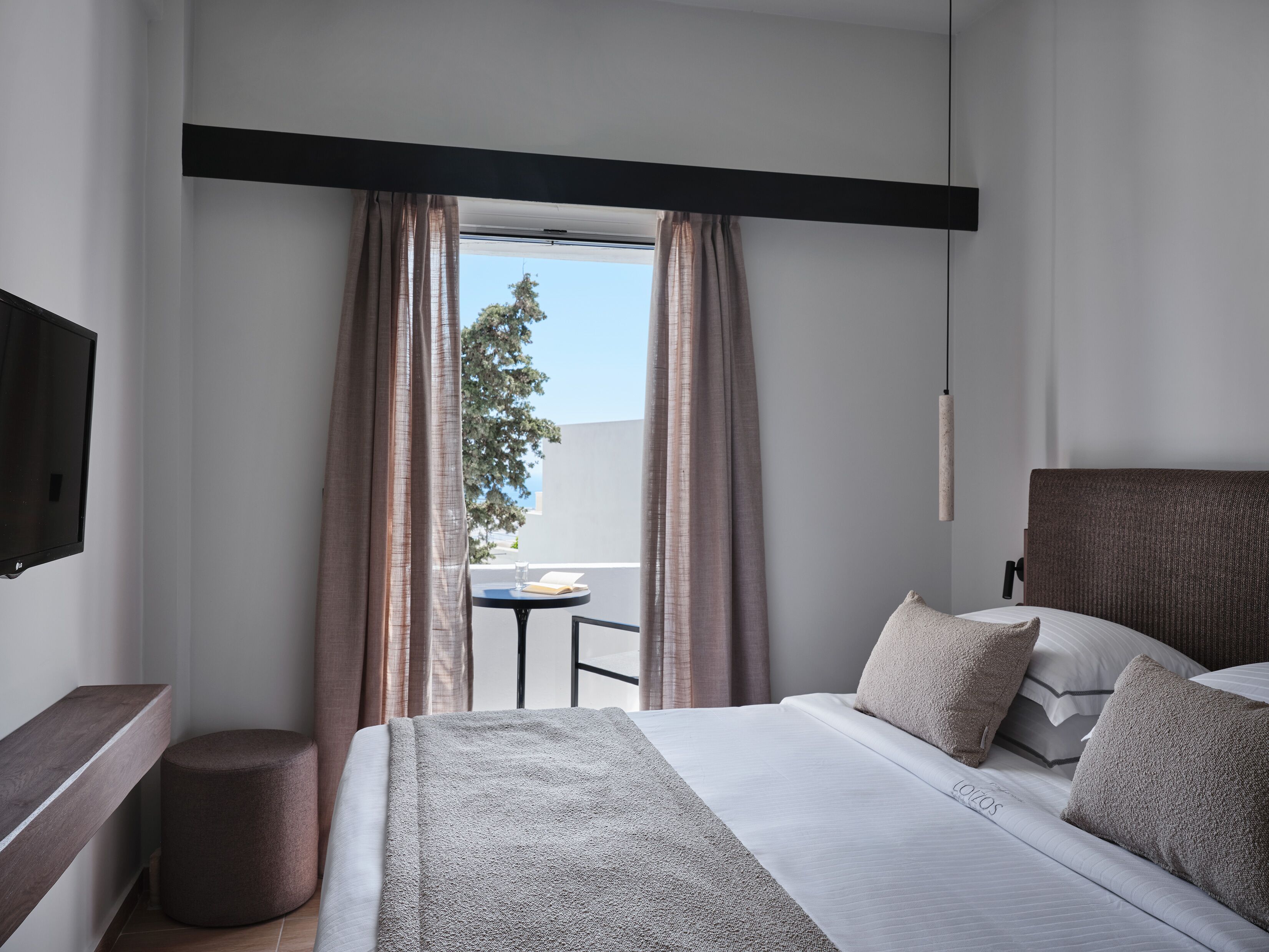 Un hotel moderno con una cama, una mesita con un libro y vistas al exterior.