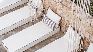 Une rangée de chaises longues blanches, agrémentées de coussins à rayures, est placée devant un mur de pierre et sur un sol en béton.
