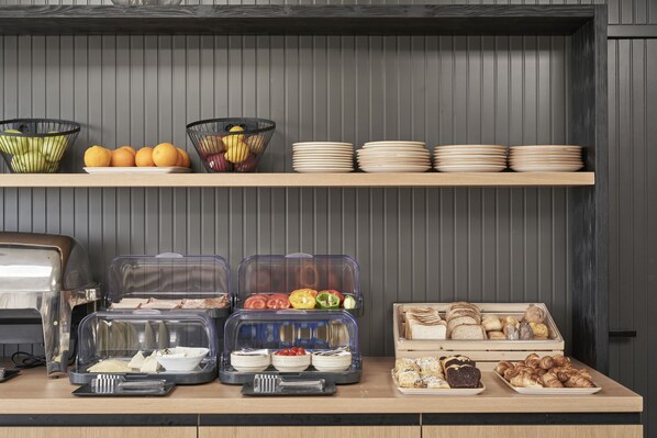 A buffet setup with various food items, including fruits, vegetables, and pastries, displayed on shelves and in containers. - Loizos Stylish Residences (Santorini)