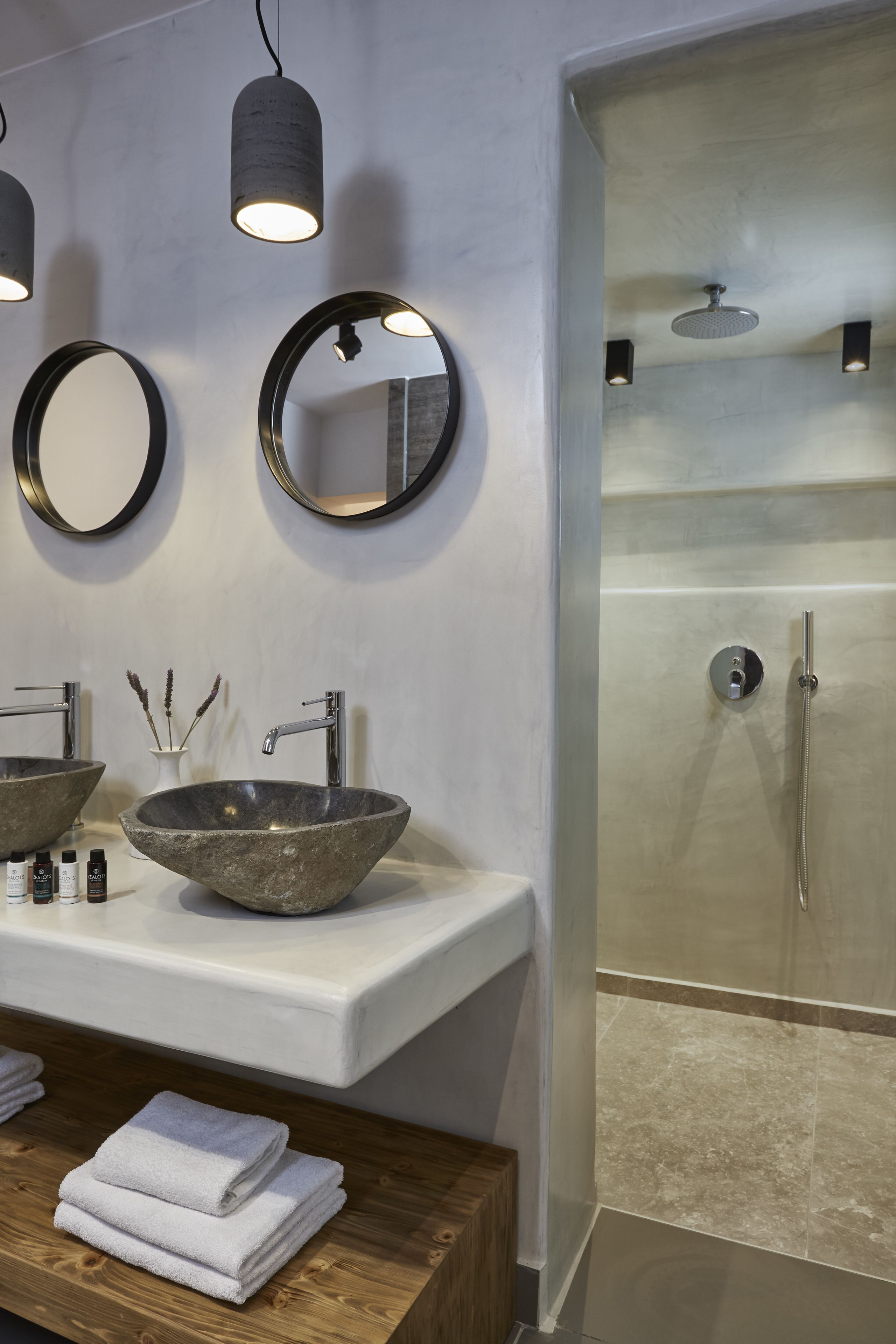 A modern bathroom with two large stone sinks, a wooden vanity, and a glass-enclosed shower.