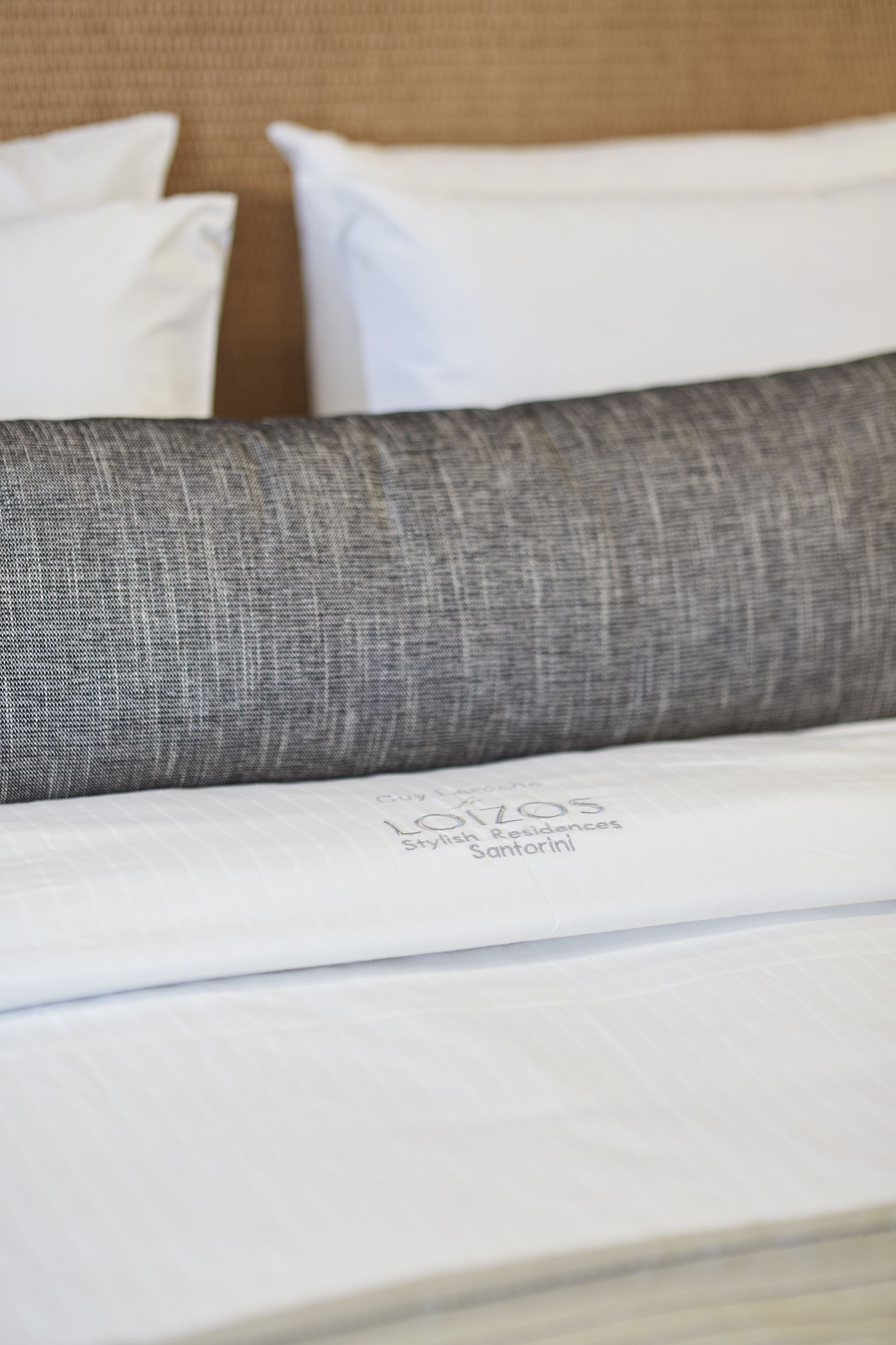 Primer plano de una cama con cabecera tapizada en gris y almohadas blancas.