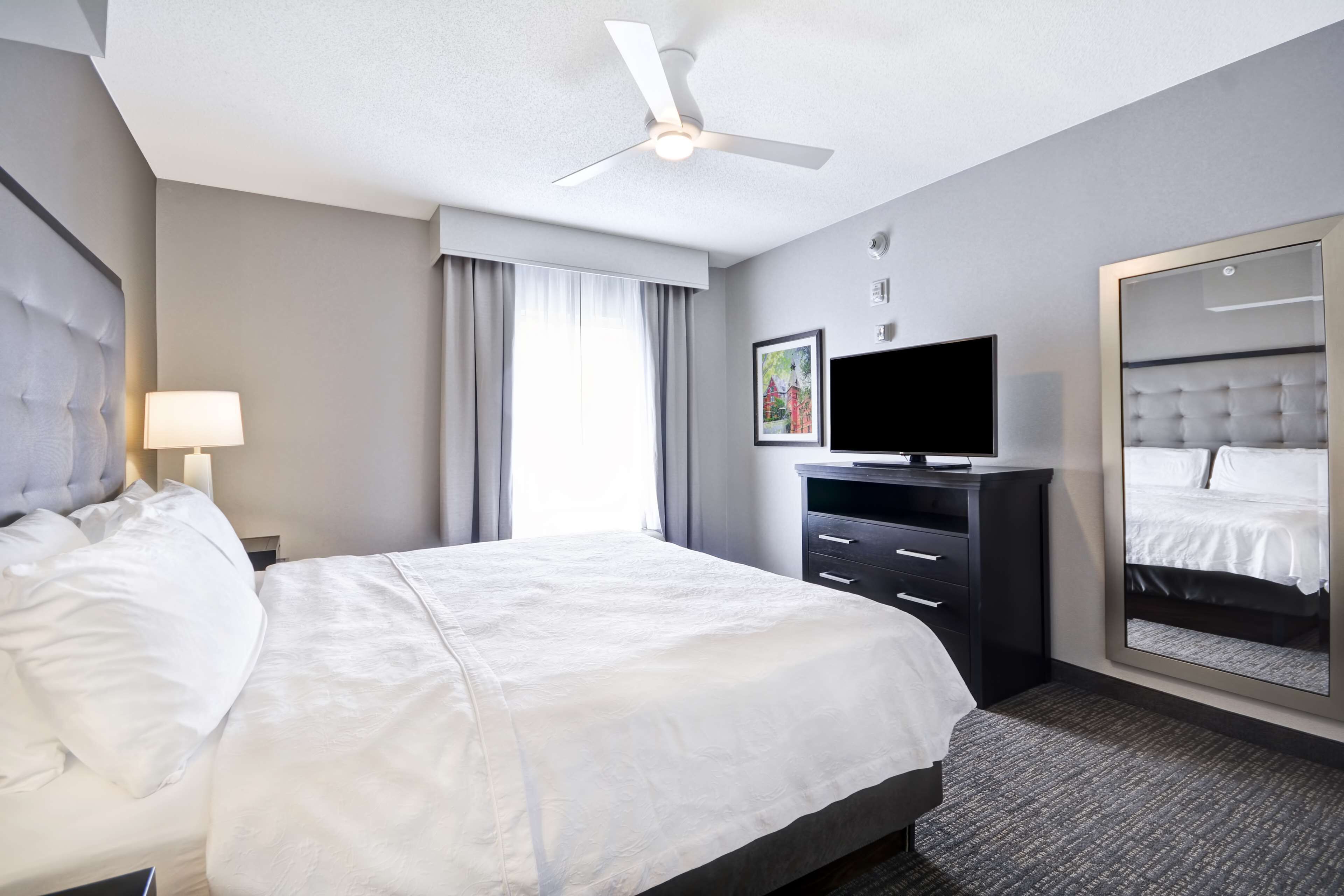 A hotel room with a large bed, a flat-screen TV, a dresser, a mirror, and a ceiling fan.