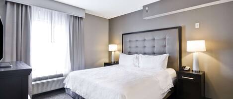 A hotel room with a large bed, two bedside tables with lamps, a ceiling fan, and a large window with curtains.