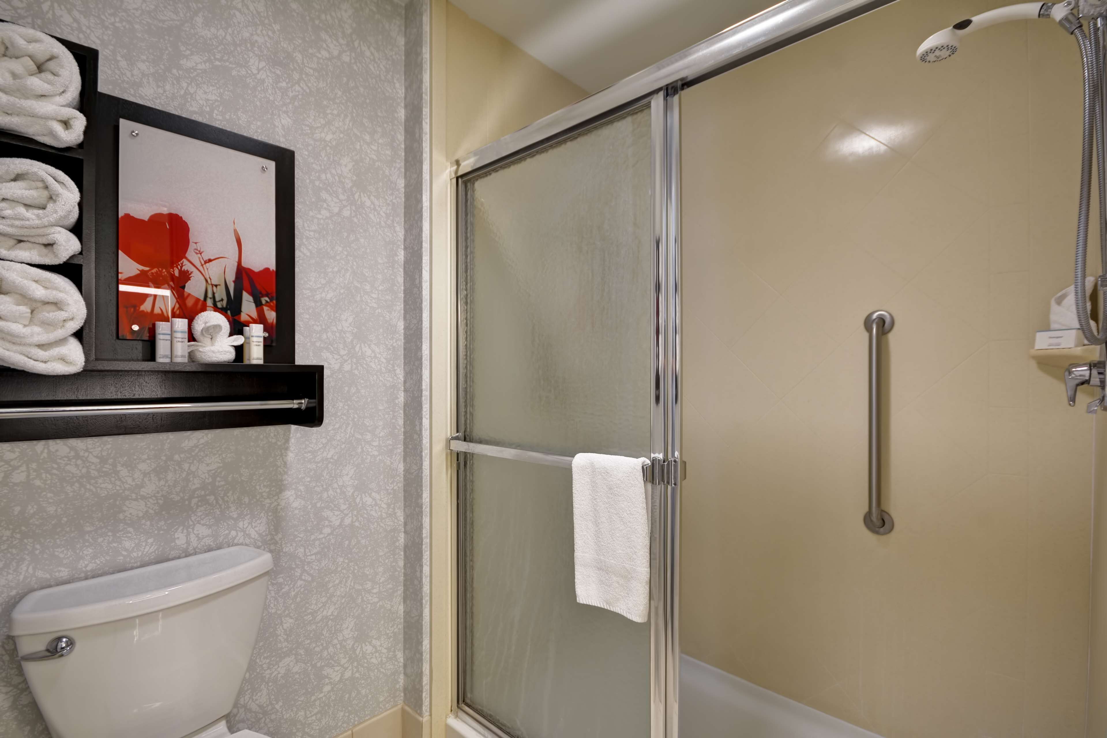 A bathroom with a toilet, a glass-enclosed shower, and a shelf with towels and toiletries.