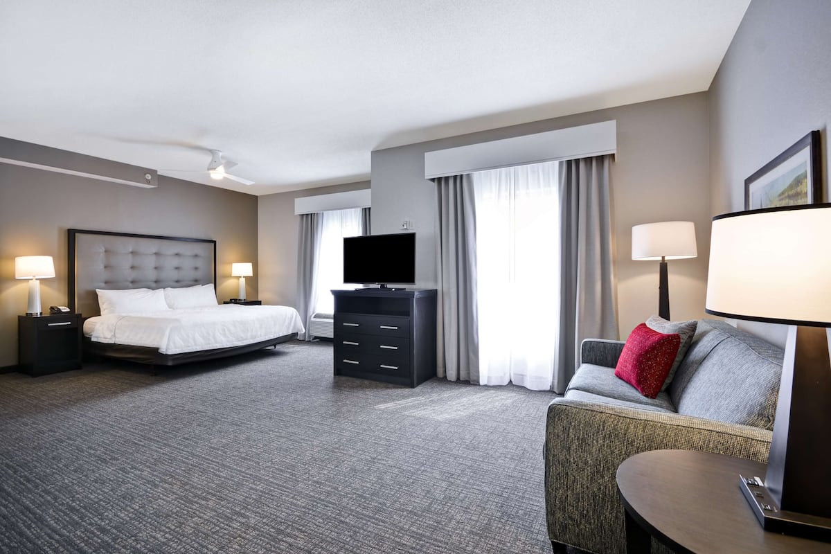 Quarto de hotel com cama, televisão, cômoda, sofá e escrivaninha.